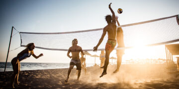 Large group of friends playing volleyball on the beach.