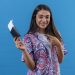 young beautiful woman tourist holding passport with tickets looking at camera pointing with index finger to them smiling cheerfully standing over isolated blue background