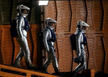 Cena de 2001: Uma Odisseia no Espaço com três astronautas em trajes prateados num ambiente de painéis alaranjados.