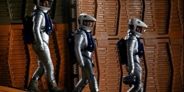 Cena de 2001: Uma Odisseia no Espaço com três astronautas em trajes prateados num ambiente de painéis alaranjados.
