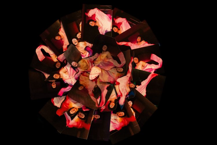 Composição circular com múltiplas imagens de pessoa envolta em tecido rosa sobre fundo preto, obra de Feio Franq