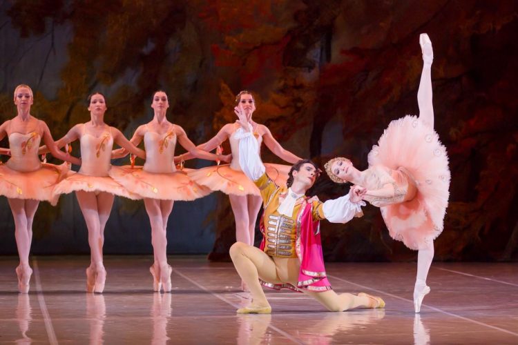 Cena de balé com bailarinos em figurinos clássicos durante apresentação de A Bela Adormecida.