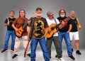 Integrantes da Banda Pra Quem Tá Quente posam com baixo, violão e instrumentos de percussão.