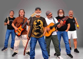 Integrantes da Banda Pra Quem Tá Quente posam com baixo, violão e instrumentos de percussão.
