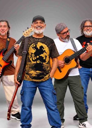 Integrantes da Banda Pra Quem Tá Quente posam com baixo, violão e instrumentos de percussão.
