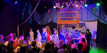 Crianças em apresentação no palco do Espaço Cultural Mapati, diante de familiares na plateia.