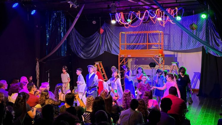 Crianças em apresentação no palco do Espaço Cultural Mapati, diante de familiares na plateia.