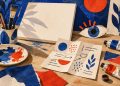 Mesa de criação artística com pincéis, tela e olho de papel; ilustração conceitual, não reproduz obras da mostra.