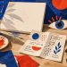 Mesa de criação artística com pincéis, tela e olho de papel; ilustração conceitual, não reproduz obras da mostra.