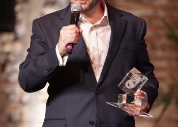 Participante da cerimônia FIAT/IFTA Awards segura um troféu e fala ao microfone na Cinemateca Brasileira.