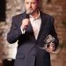 Participante da cerimônia FIAT/IFTA Awards segura um troféu e fala ao microfone na Cinemateca Brasileira.