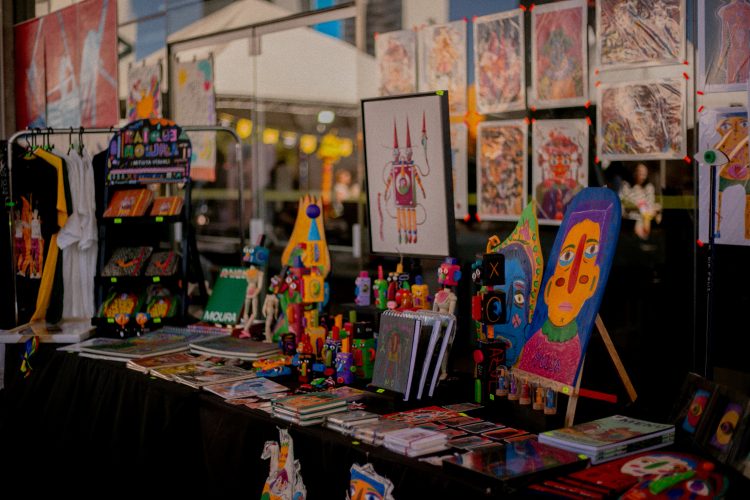 Estande da Feira MOTIM com livros, ilustrações, brinquedos artísticos e obras de arte impressa
