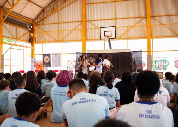 Estudantes apresentam uma cena diante da comunidade escolar, em uma quadra coberta, no projeto de leitura dramatizada no DF.