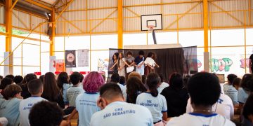 Estudantes apresentam uma cena diante da comunidade escolar, em uma quadra coberta, no projeto de leitura dramatizada no DF.
