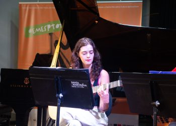 Violonista toca durante a Revirada Musical da EMESP Tom Jobim, com piano e estante de partituras no palco.