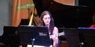 Violonista toca durante a Revirada Musical da EMESP Tom Jobim, com piano e estante de partituras no palco.