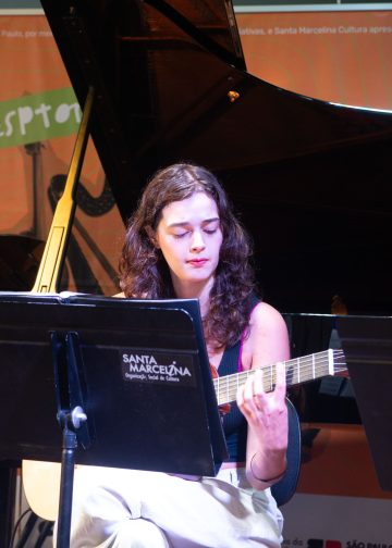 Violonista toca durante a Revirada Musical da EMESP Tom Jobim, com piano e estante de partituras no palco.