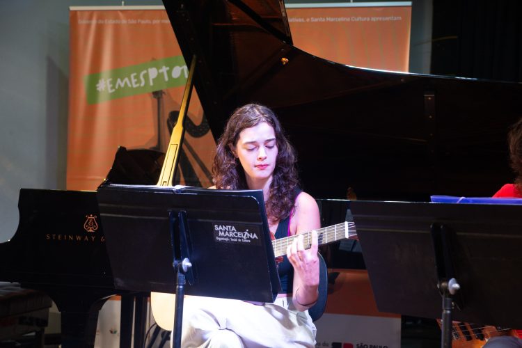 Violonista toca durante a Revirada Musical da EMESP Tom Jobim, com piano e estante de partituras no palco.