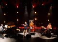 Teco Cardoso Quarteto no palco, com flauta, piano, contrabaixo e bateria, sob iluminação em tons quentes.