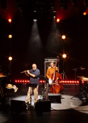 Teco Cardoso Quarteto no palco, com flauta, piano, contrabaixo e bateria, sob iluminação em tons quentes.