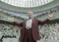 Tom Cruise como Digger Rockwell, de terno vinho e braços abertos diante de uma plateia.