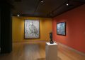 Vista da exposição de Vik Muniz no CCBB Rio de Janeiro, com fotografias em paredes amarelas e vermelhas e escultura sobre pedestal.