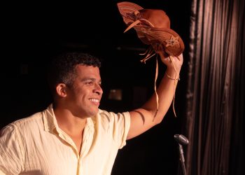 Wêlson Nunes sorri no palco, com um microfone na mão e um chapéu de couro erguido.